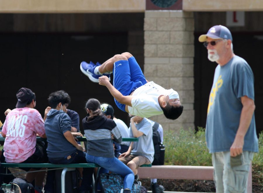 Ocean Park, freshman, performs back flips in the quad as staff member Kevin ODea observes the lunchtime crowds. The week of Aug. 16 to Aug. 20 marked the first time in 17 months that the entire student body had access to the quad for lunch.