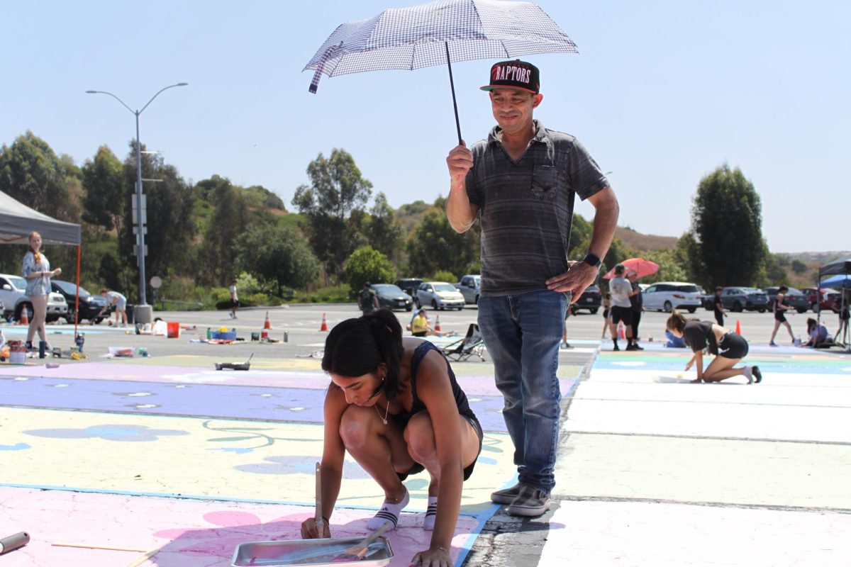 As her father provides shade from the sun, Clarissa Ricalde paints floral patterns on her senior parking spot. Seniors, with the help of family and friends, spent the weekend personalizing parking spots in the lower lot.