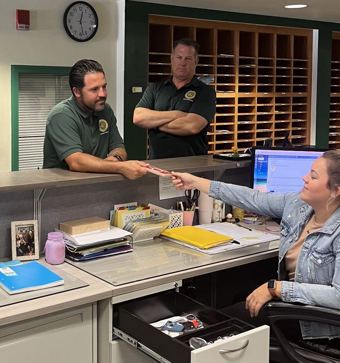 Tanner Eliot and Bob Till, campus supervisors, hand a confiscated cell phone to Michelle Garcia, administrative assistant. The new phone policy was implemented to combat rampant cell phone usage in classrooms.
