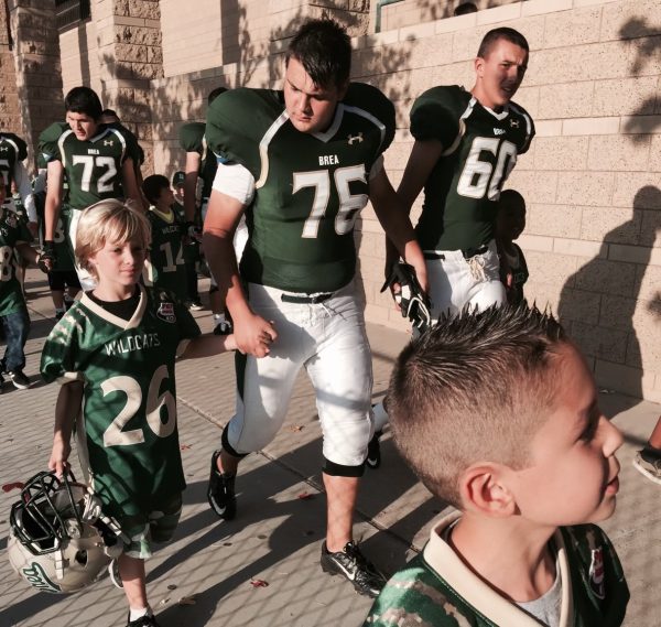 Jonathan Ruiz ('25), left, leads Ryan Seymour ('17) into Wildcat Stadium before a varsity football game in 2016. Ruiz is one of 37 players on this year's varsity roster that played in the Pop Warner youth league. (Courtesy of Kelly Mason.)