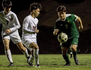 Max Velazquez ('25) powers past a pair of Troy defenders during boys' varsity soccer's league-opening win on Jan. 6. 