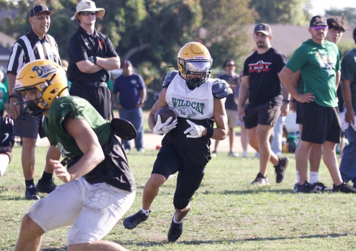 Running back Jio Kang ('27) heads upfield as varsity head coach Justin Villasenor, right, looks on. 
