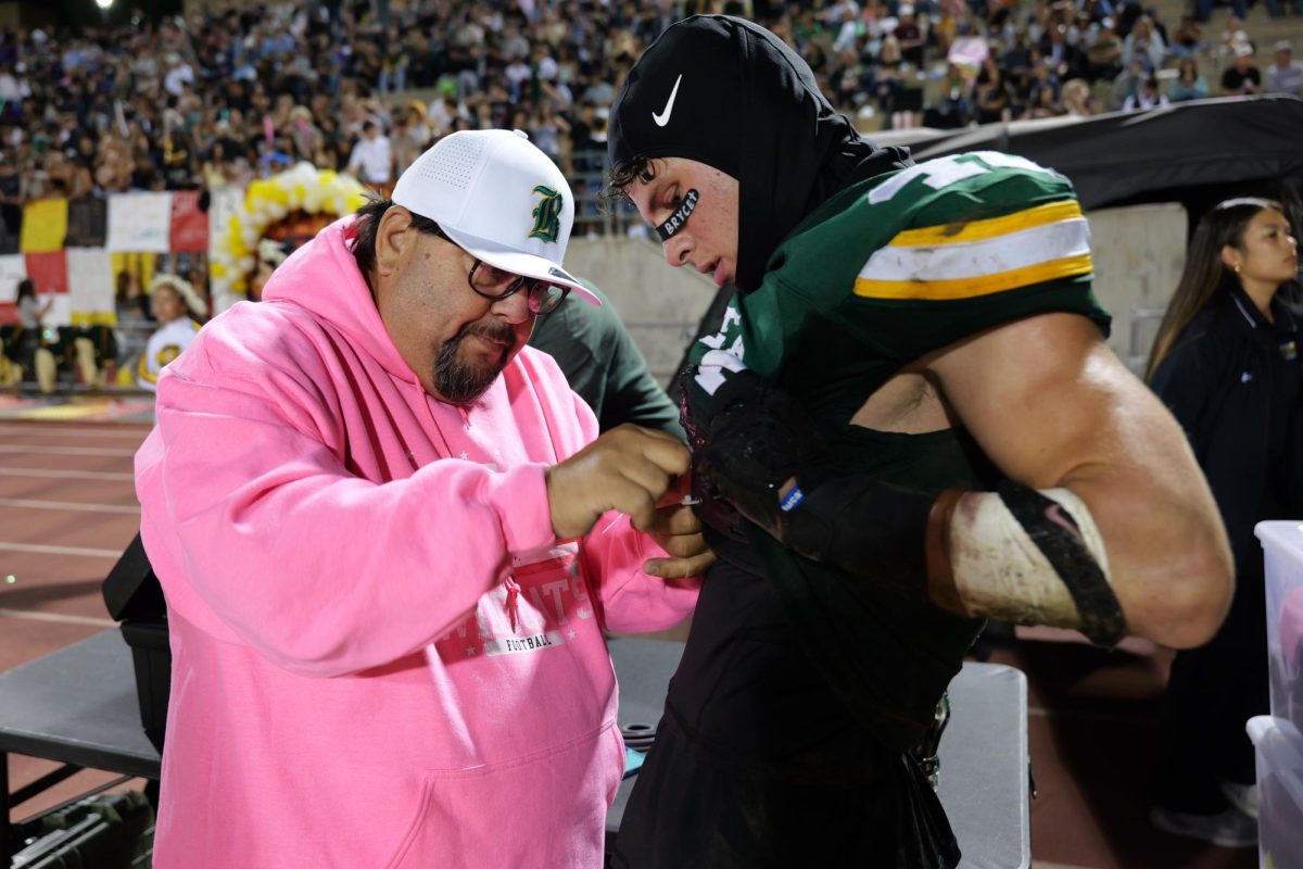Eric "Zeke" Zeker re-strings outside linebacker Nick Davis's pads during a game against St. Margaret's High School Oct. 10. For 25 years, Zeke has served as BOHS's equipment manager.
