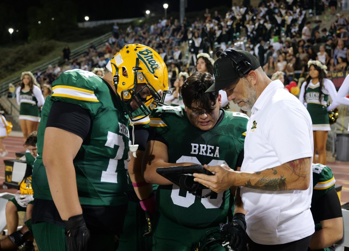 Defensive line coach J.D. Senkbile discusses play with Jacob Vega ('26) and Jesse Jimenez ('28) on the sidelines of the varsity football game Oct. 10.